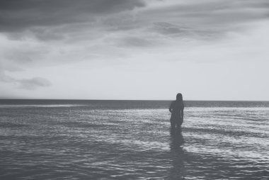 Gün batımında denizde yürüyen genç kadın silüeti