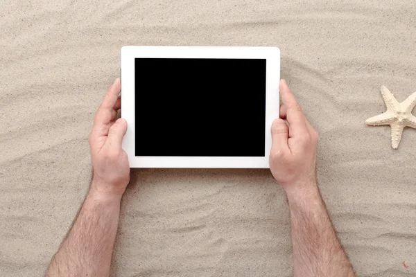 Man holding tablet with blank screen lying on sand — Stock Photo, Image