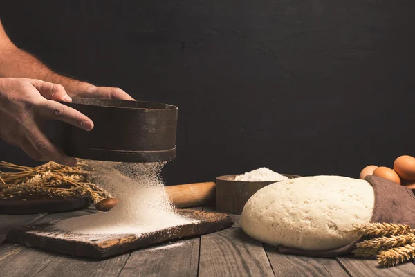 Baker sifts prostřednictvím mouky na dřevěný stůl — Stock fotografie