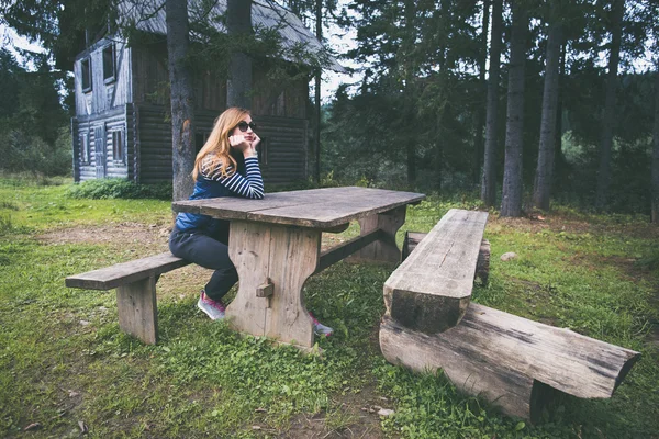 Женщина сидит за столом рядом со старым деревянным домом — стоковое фото
