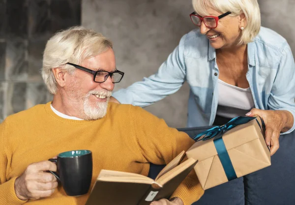 Happy elderly exchange gifts. Joyful seniors couple is having a holiday together. Birthday concept or anniversary concept