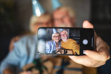 Yaşlı adam karısıyla selfie çekiyor. Evde hediyelerle doğum gününü kutluyoruz.