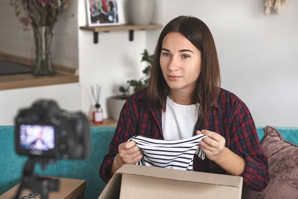 Caucasian female vlogger opens package and records live video of unpacking things at home for subscribers
