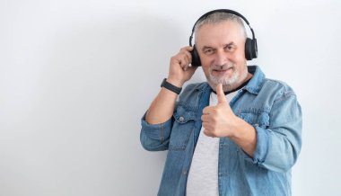 Sakallı, kablosuz kulaklık takan modern yaşlı adamın portresi. Çok komiktir ve baş parmağını kaldırır.