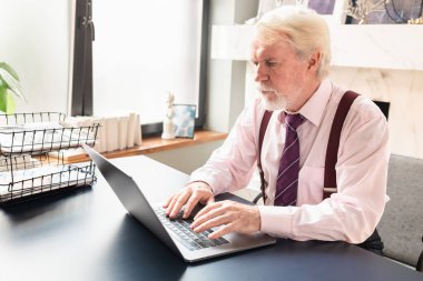 Evde dizüstü bilgisayarla çalışan yaşlı bir adam.