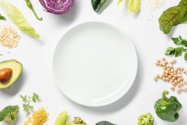 Beyaz arka planda beyaz tabağın etrafına taze sebzeler çerçevele. Üst görünüm