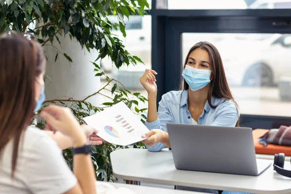 Two employees sit in masks observing social distancing under quarantine