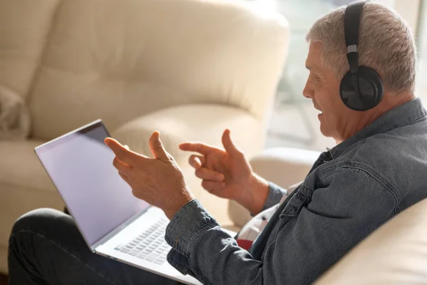 Senior elderly man sitting on sofa at home using online technology to talk to family or friends. An elderly man communicates via video conference with his loved ones