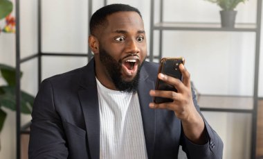 Genç Afrikalı Amerikalı iş adamı ya da öğrenci akıllı telefondan beklenmedik iyi haberler okuyor.