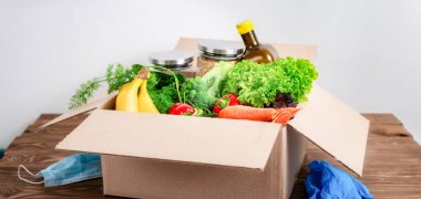 Yemek teslimatı ya da bağış konsepti. Eldivenli ve koruyucu maskeli ahşap masada bir kutu yemek.