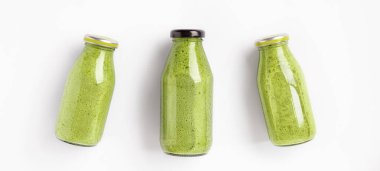 Beyaz arka planda üç şişe yeşil meyve püresi. Sağlıklı ve lezzetli yemekler.