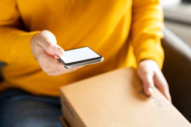 Evden alışveriş ve eve teslimat konsepti. Evde boş ekranlı akıllı telefonu tutan kadın.