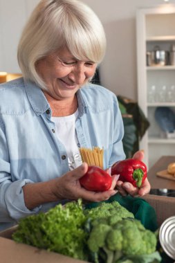 Yemek teslimatı ya da bağış konsepti. Mutlu yaşlı kadın gönüllülerden bir kutu yiyecek aldı.