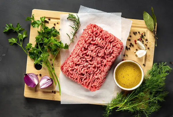 Koyu arkaplanda kesilmiş taze kıyma ve üst manzara için malzemeler var.
