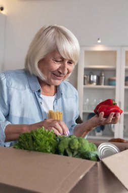 Yemek teslimatı ya da bağış konsepti. Mutlu yaşlı kadın gönüllülerden bir kutu yiyecek aldı.