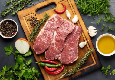 Koyu arkaplanda taze et ve üst görüntüde pişirmek için malzemeler var.