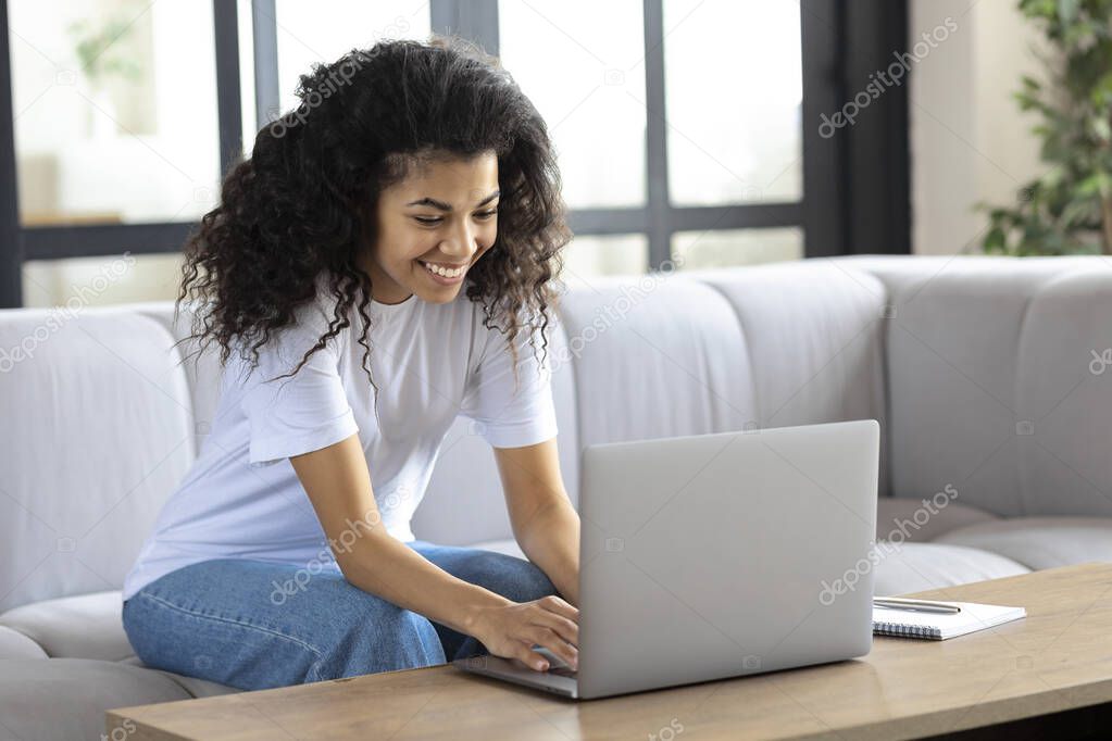 Young successful african american woman sitting at home on the couch streaming something on a laptop