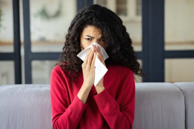 Grip olmuş Afrikalı Amerikalı bir kadın evdeki kanepede oturarak burnunu temizliyor. Soğuk, grip konsepti