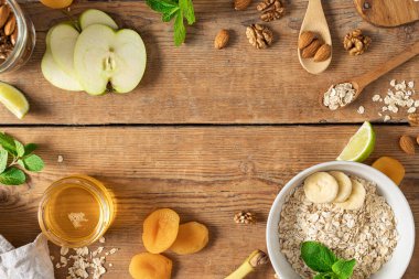 Sağlıklı kahvaltı hazırlamak için gerekli malzemelerin çerçevesi. Yulaf ezmesi, kurutulmuş taze meyve, bal ve fındık, ahşap masa manzaralı. Kahvaltı masası konsepti
