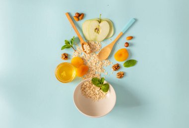 Sağlıklı kahvaltı hazırlamak için gereken malzemeler yulaf ezmesi, kuru meyve, bal ve fındık ve mavi arka planda. Kahvaltı masası konsepti