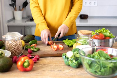 Genç bir kadın ev mutfağındaki taze sebzelerden sağlıklı bir kahvaltı veya akşam yemeği hazırlıyor. Sağlıklı yaşam tarzı ve sağlıklı gıda konsepti