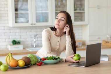 Genç beyaz kadın mutfakta elinde yeşil bir elmayla dikiliyordu. Sağlıklı yaşam tarzı ve sağlıklı gıda konsepti