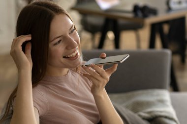 Güzel, genç, beyaz bir kadın evinde kanepede otururken cep telefonuyla hoş sohbetler ediyor.