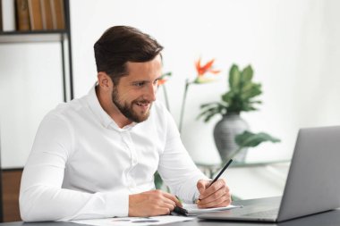 Bilgisayarlı ekrana bakıp gülümseyen yakışıklı genç adam ev ofisinde otururken, çevrimiçi eğitim veya eğitimdeyken başarılı bir iş adamı video konferansında bir koçla iletişim kuruyor.