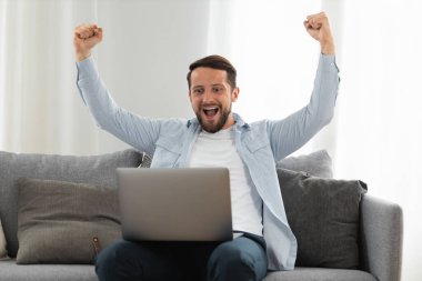 Dizüstü bilgisayarı olan neşeli ve şaşırmış genç adam, evdeki kanepede otururken yeni bir iş bulduğu için seviniyor. Erkek öğrenci piyangoyu kazanmakla ilgili bir e-posta aldığı için kendini şanslı hissediyor.