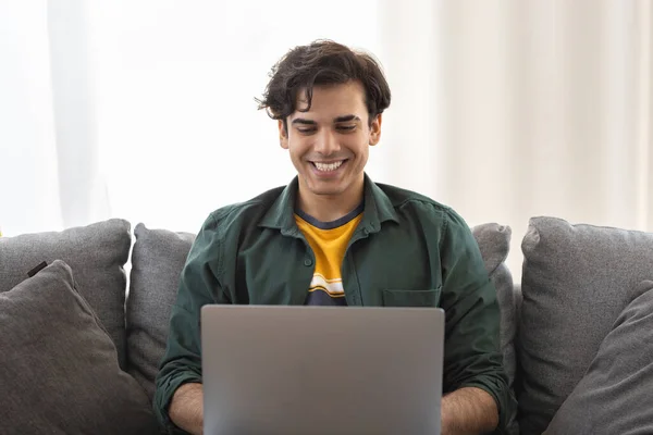 Joven Hombre Alegre Sentado Sofá Con Ordenador Portátil Interior Mirando —  Fotos de Stock