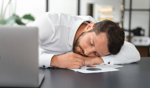 Уставший бизнесмен спит за своим столом после длительного анализа отчета о продажах, хронического отсутствия сна
