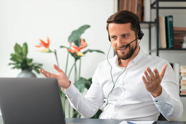 Friendly caucasian man, office worker or consultant support services, uses a headset and laptop for online consultation or negotiation, video call