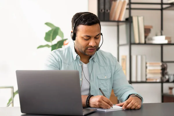 Hombre Indio Joven Auriculares Tomando Notas Cuaderno Mientras Webinar Línea —  Fotos de Stock