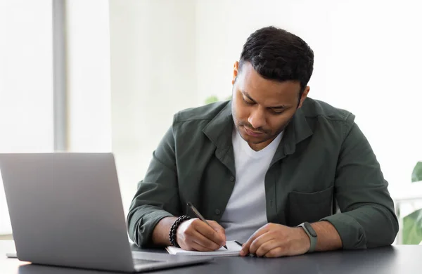 Hombre Indio Concentrado Tomando Notas Mientras Está Sentado Mesa Con —  Fotos de Stock