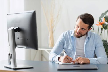 Genç Kafkasyalı serbest çalışan ya da dizüstü bilgisayara bakarak not alan bir öğrenci evde konsept uzaklık eğitiminde internetten ders çalışıyor.