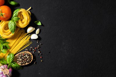 Italian food ingredients with pasta, tomatoes, pepper, garlic and parsley on dark background with copy space, top view
