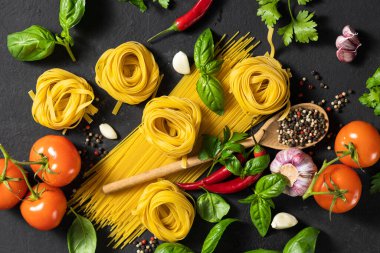 Set of various ingredients for making Italian pasta, noodles. Spaghetti and tagliatelle with tomatoes, pepper, garlic and parsley on dark background, top view