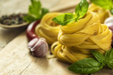 Tagliatelle with basil, pepper, garlic and parsley on wooden table close up with copy space