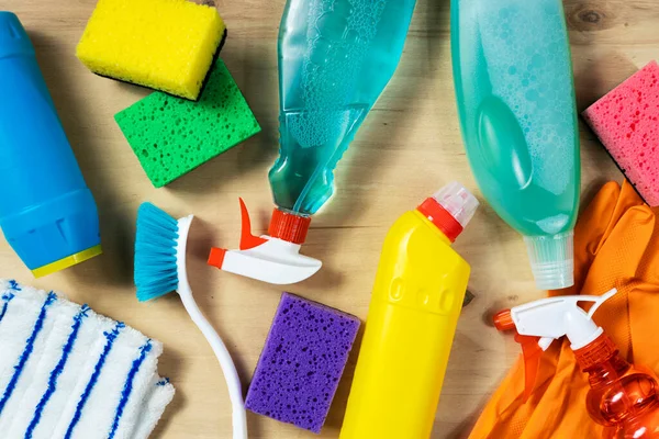 Various cleaning supplies, sprays, bottles, sponge, rubber gloves on wooden background, top view. Cleaning concept