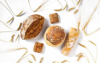 Bakery. Set of freshly baked crispy bread and buns with ears of wheat on white background top view, flat lay