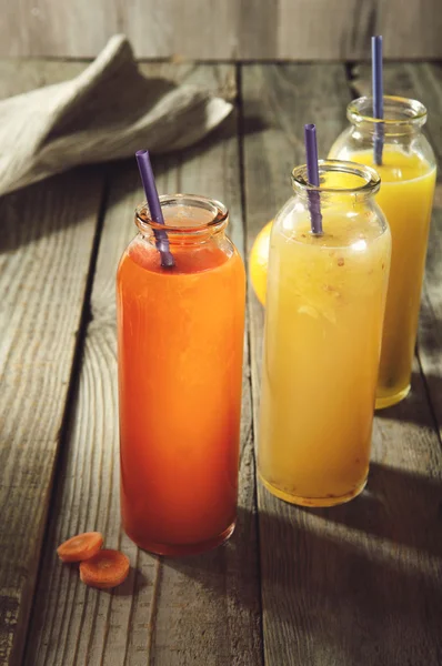 Frischer Saft in Flaschen auf dem alten Holzgrund. Apfelsaft, Karottensaft, Orangensaft — Stockfoto