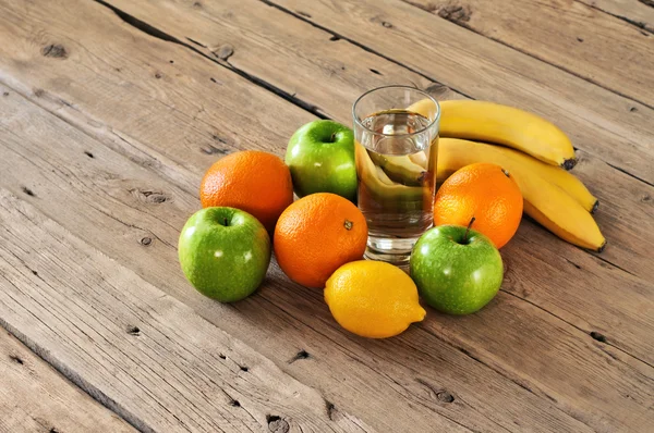 Fruto com um copo de água em uma mesa de madeira — Fotografia de Stock