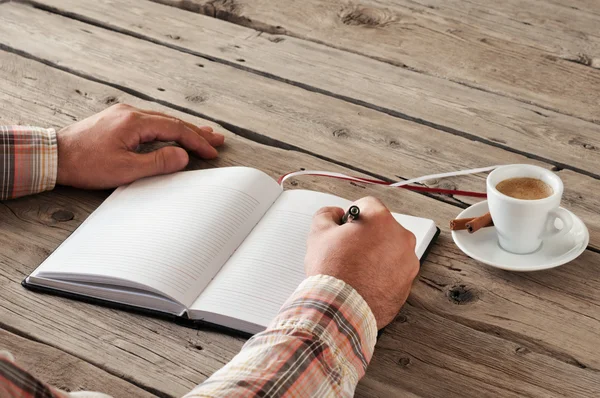 Mão de homem escrevendo algo em caderno em branco na mesa de madeira — Fotografia de Stock