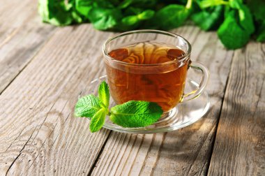 Cam bardak çay ile bir daire bir ahşap masa portre üzerinde bir nane yaprağı