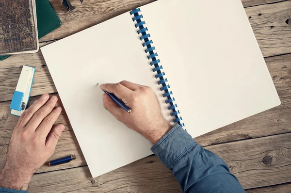 Schreibt der Mann in ein offenes Notizbuch mit leeren Seiten auf hölzernem Papier — Stockfoto