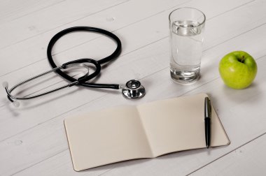 Open notebook with pen, stethoscope, apple and a glass water clipart