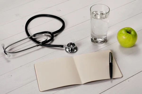 Taccuino aperto con penna, stetoscopio, mela e acqua di vetro — Foto Stock
