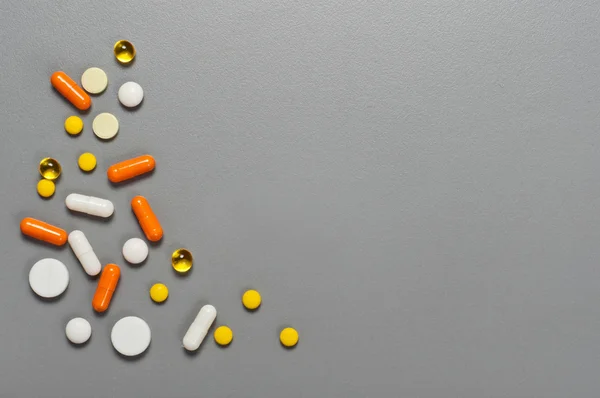 Derramando pílulas e cápsulas em um fundo cinza close-up — Fotografia de Stock
