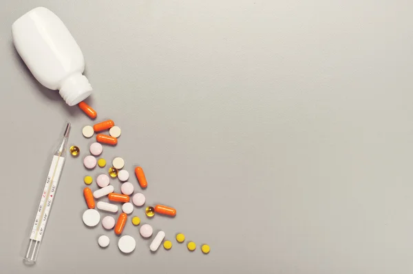 Pillole e capsule fuoriuscite dal flacone con termometro — Foto Stock