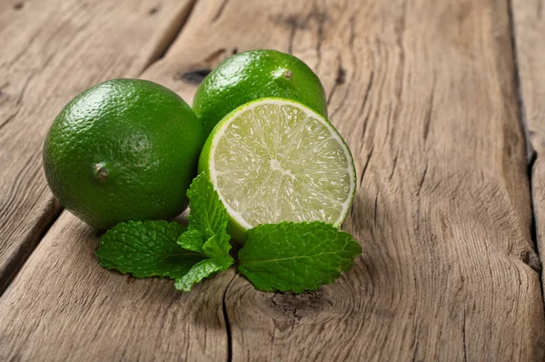 Fresh limes with mint leaves on wooden table — Stok fotoğraf